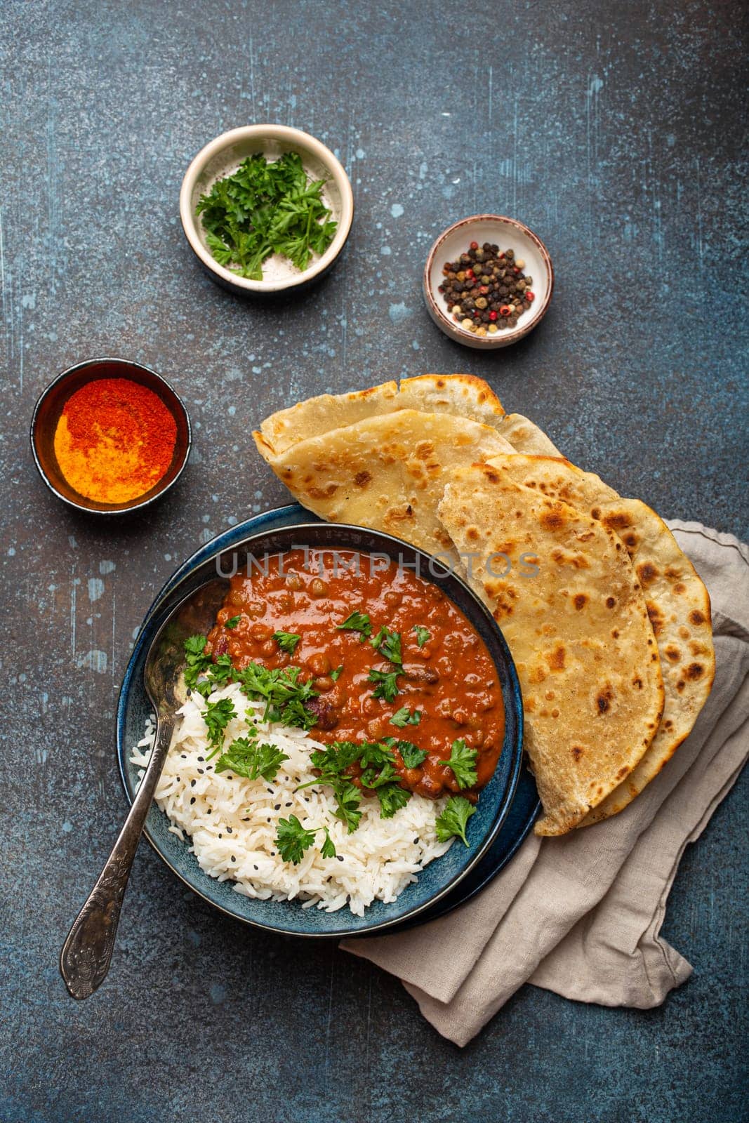 Traditional Indian Punjabi dish Dal makhani with lentils and beans in black bowl served with basmati rice, naan flat bread, fresh cilantro and spoon on blue concrete rustic table top view.