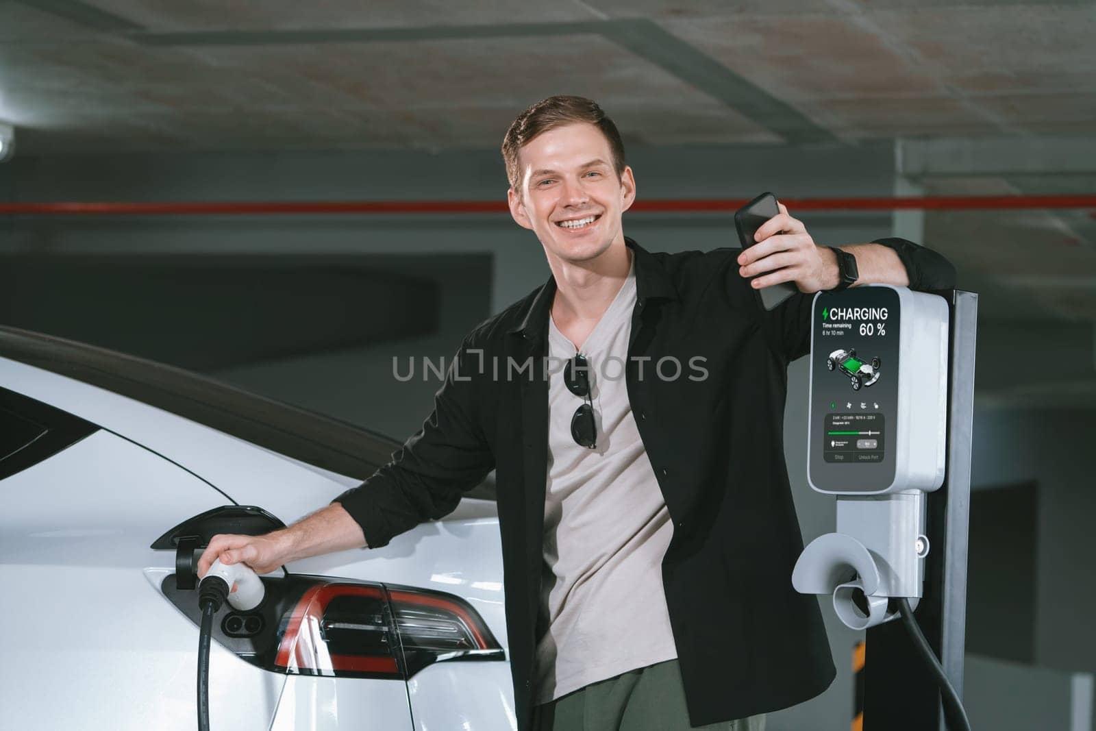 Young man travel with EV electric car to shopping center parking lot charging in downtown city showing urban sustainability lifestyle by green clean rechargeable energy of electric vehicle innards