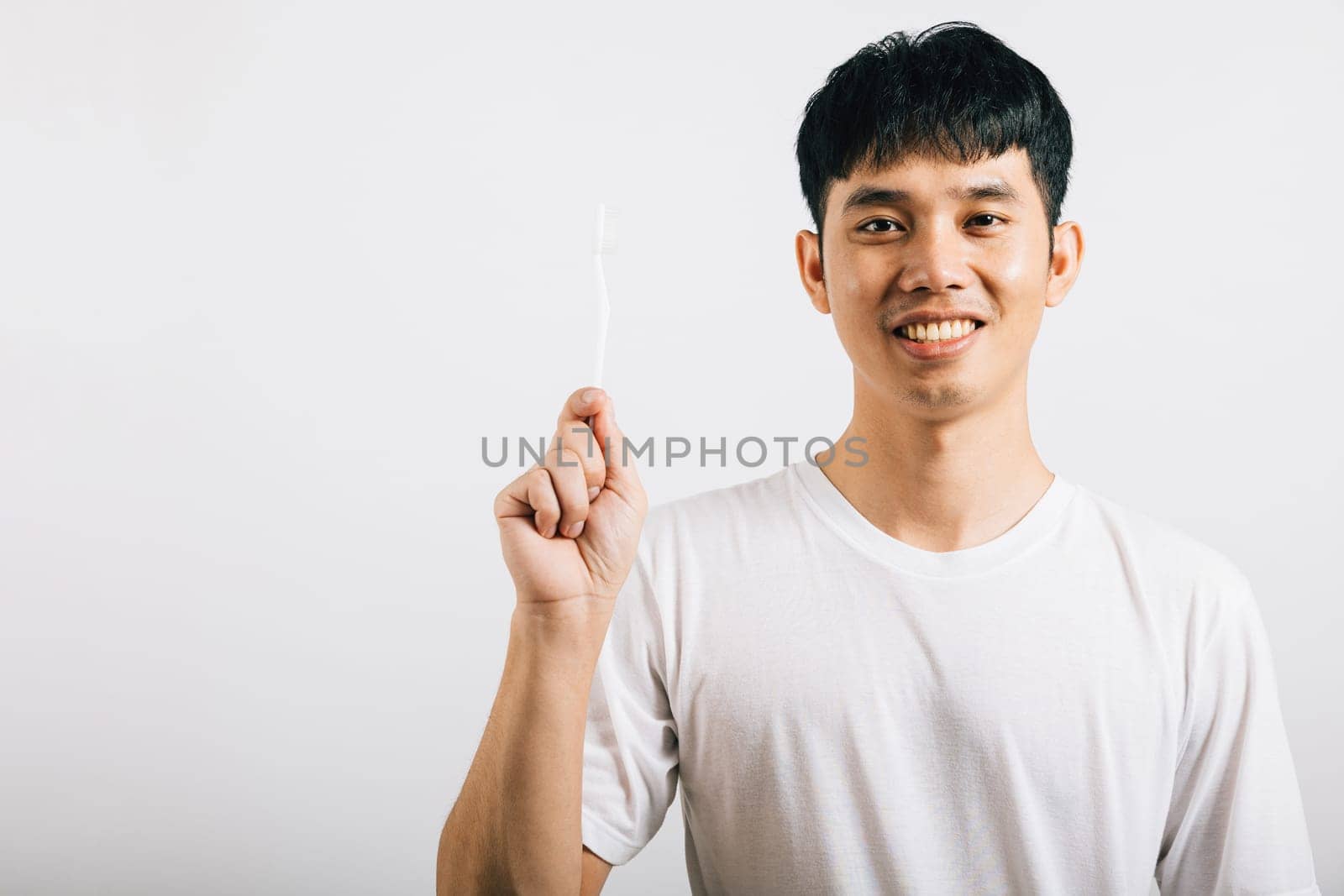 Asian young man demonstrates proper toothbrushing for dental health with a confident smile by Sorapop