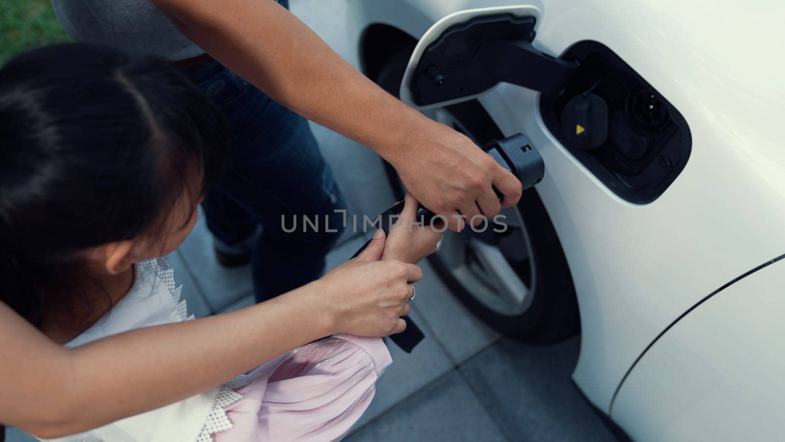 Progressive parents with electric vehicle and home charging station. Happy family with daughter giving each other high fives before leave for school. Alternative future transportation concept of EVs