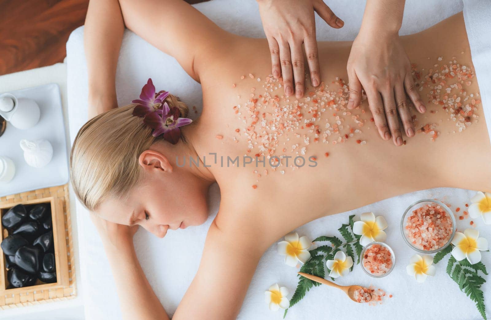 Panorama top view woman customer having exfoliation treatment in luxury spa salon with warmth candle light ambient. Salt scrub beauty treatment in health spa body scrub. Quiescent