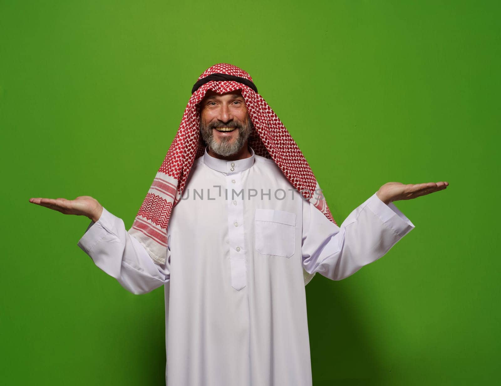 Muslim man holds two hands in gesture against green background, with empty blank copy space for text. Concept of choice and decision-making, man's contentment reflects satisfaction of making decision. High quality photo