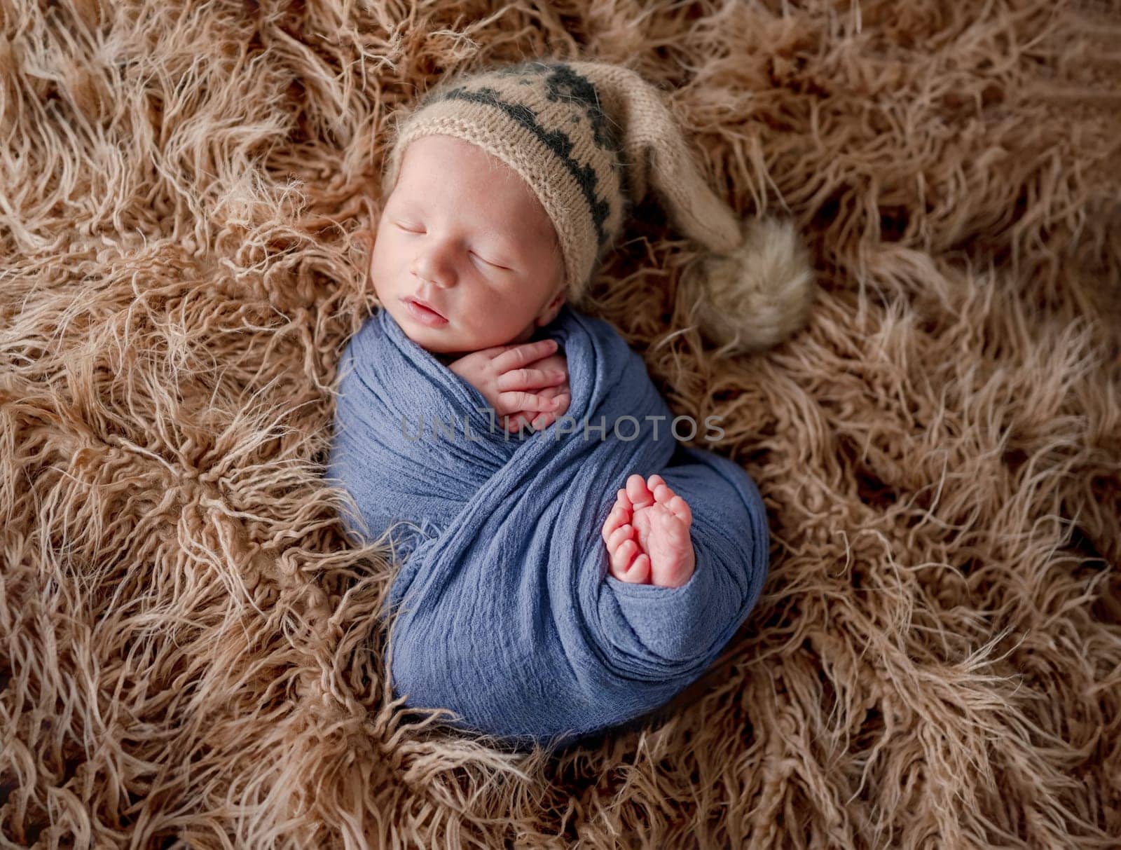 Adorable newborn baby boy smiling during sleeping and holding knitted giraffe toy. Cute infant child kid napping on fur