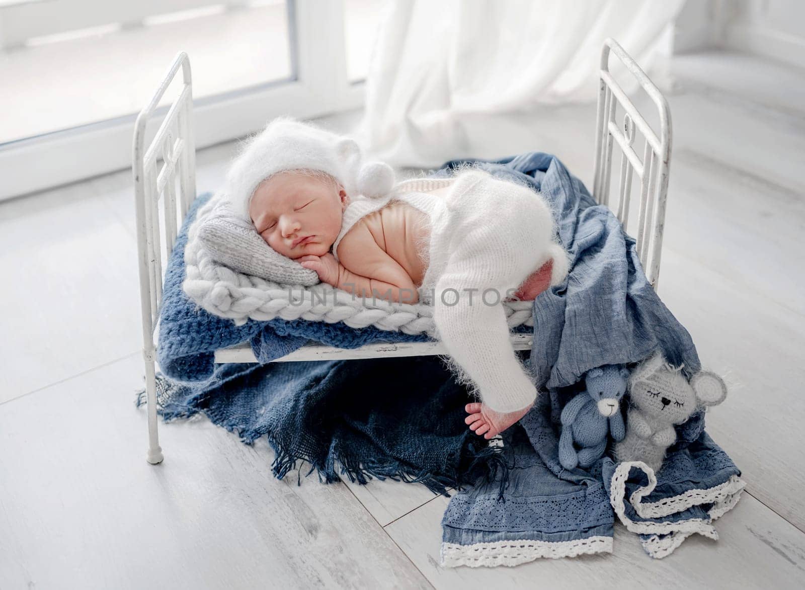 Adorable newborn baby boy sleeping in tiny bed decorated with blankets and knitted toys. Cute infant child kid napping in white warm clothes