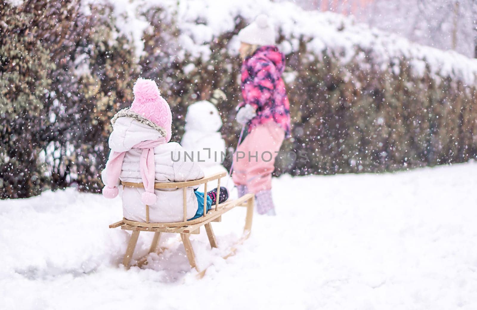 Girl sledding her sister in snow park. Family vacation in winter. High quality photo