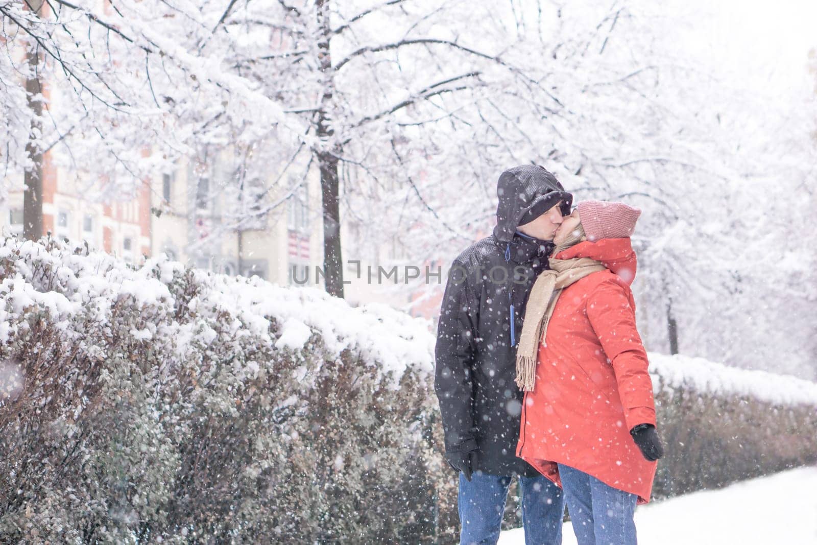 Happy amorous couple hugging each other and kissing at snow day in winter park. High quality photo