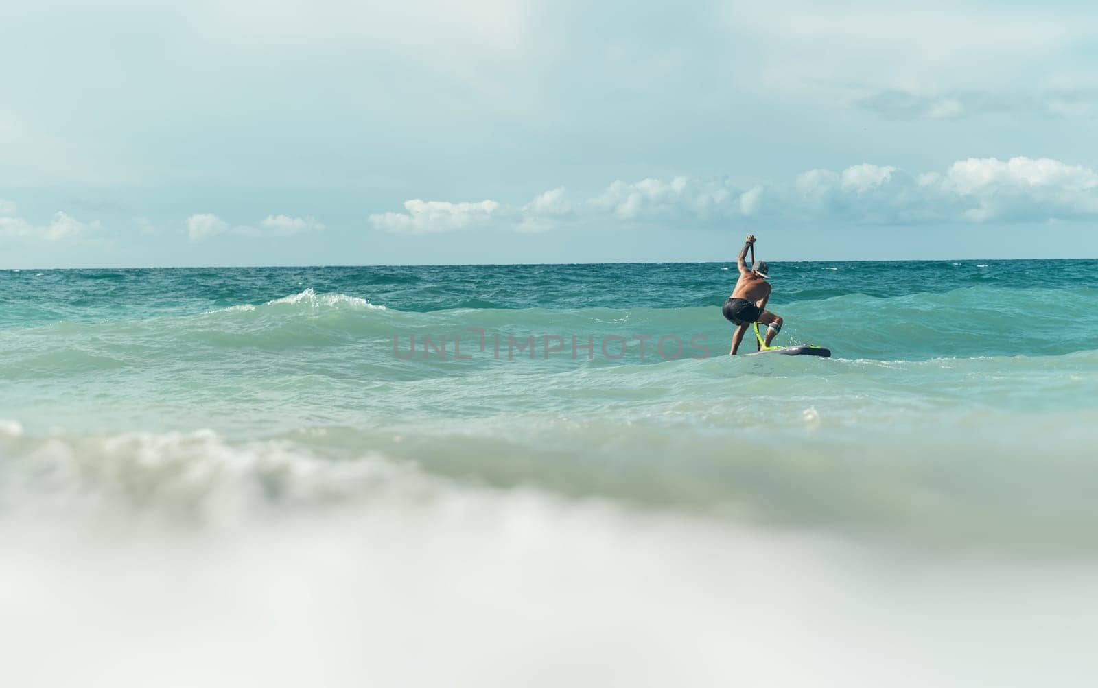 athletic wiry surfer guy swims with a paddle on a sup board in the sea