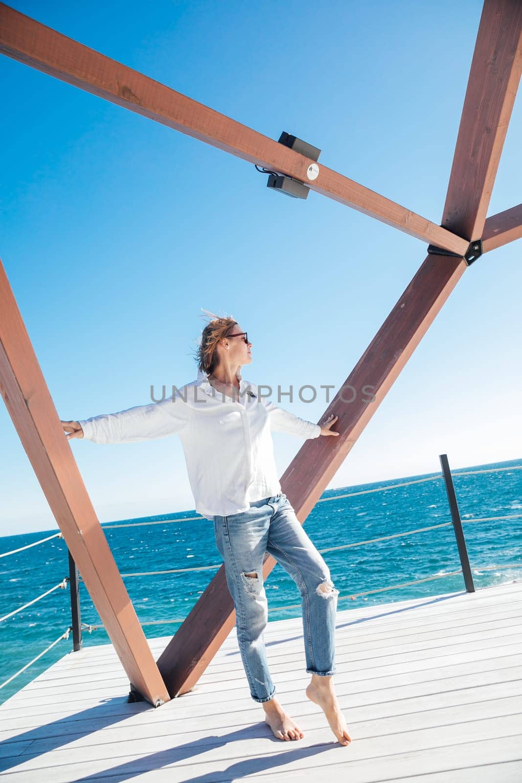 a woman in jeans stands near a wooden frame on the sea