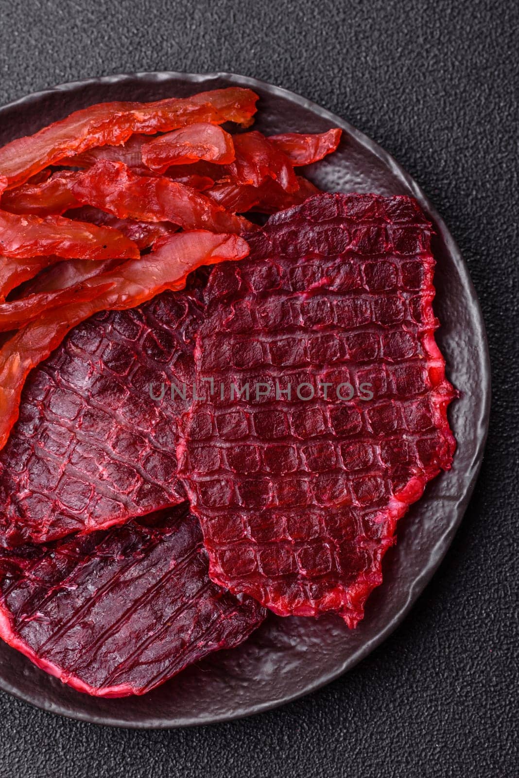 Dried beef slices, jerky, with cherry or plum flavor, salt and spices on a dark concrete background