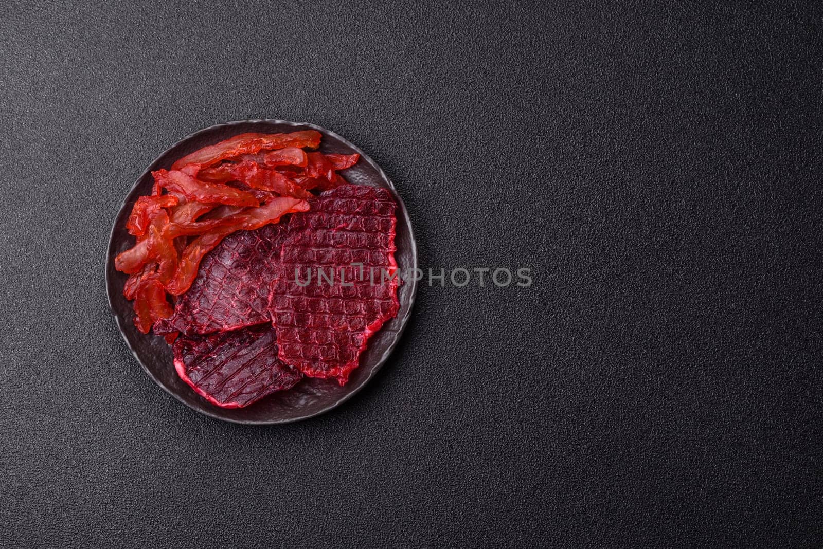 Dried beef slices, jerky, with cherry or plum flavor, salt and spices on a dark concrete background