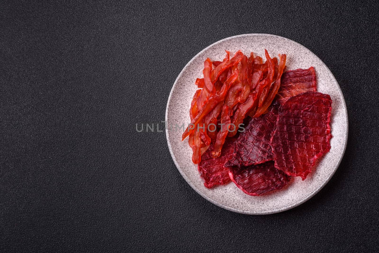 Dried beef slices, jerky, with cherry or plum flavor, salt and spices on a dark concrete background