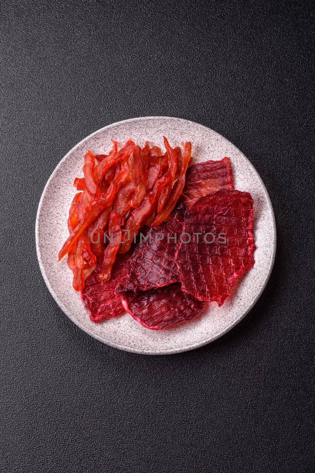 Dried beef slices, jerky, with cherry or plum flavor, salt and spices on a dark concrete background