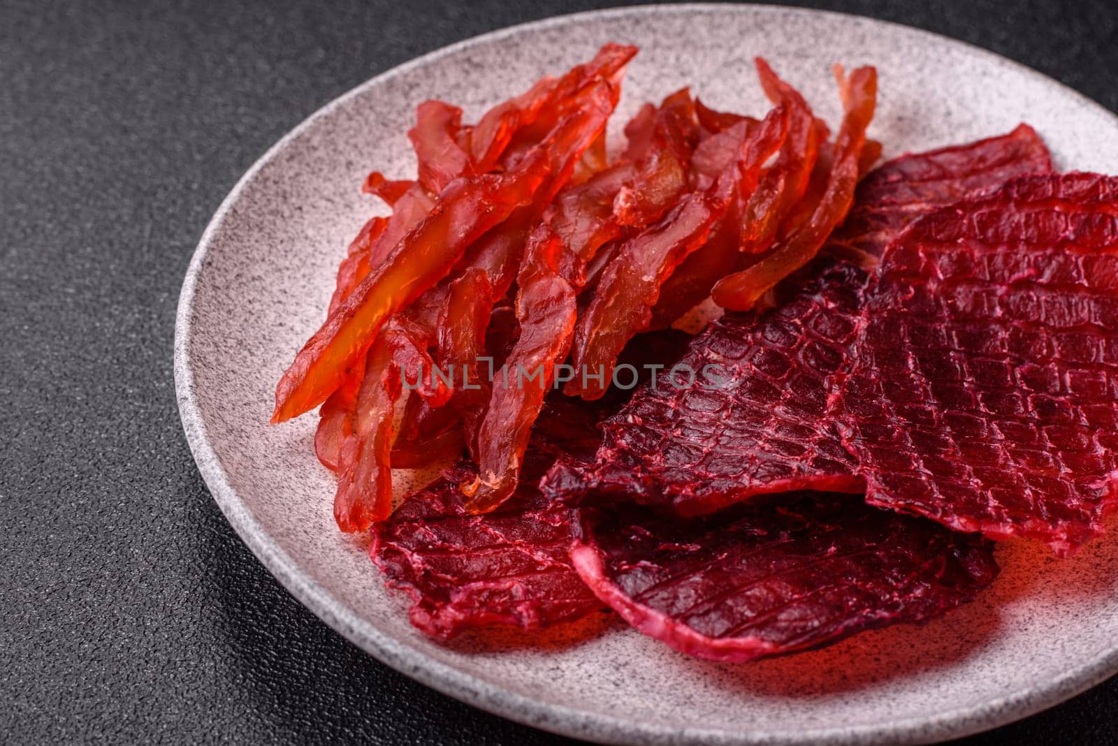 Dried beef slices, jerky, with cherry or plum flavor, salt and spices on a dark concrete background