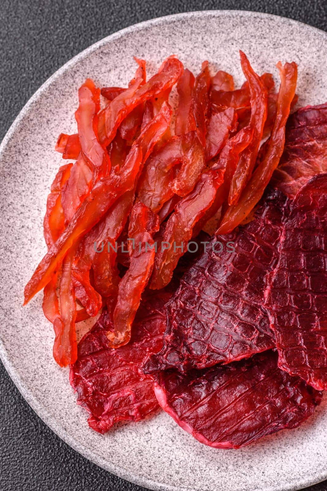 Dried beef slices, jerky, with cherry or plum flavor, salt and spices on a dark concrete background