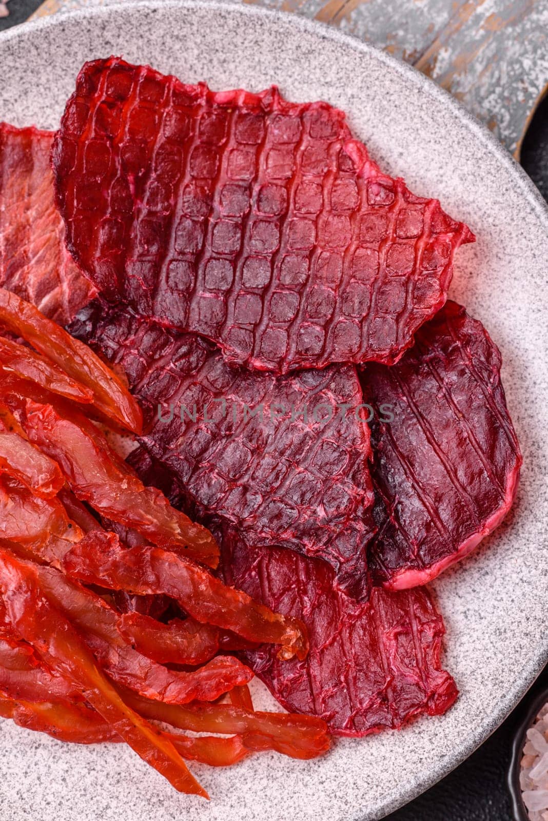 Dried beef slices, jerky, with cherry or plum flavor, salt and spices on a dark concrete background