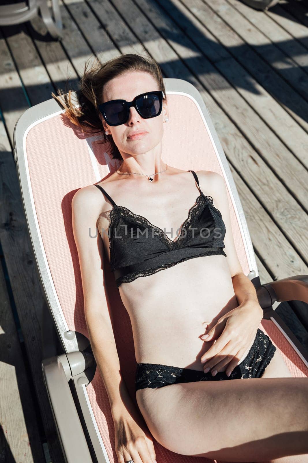 woman in a black swimsuit lies on a chaise longue on the beach rest