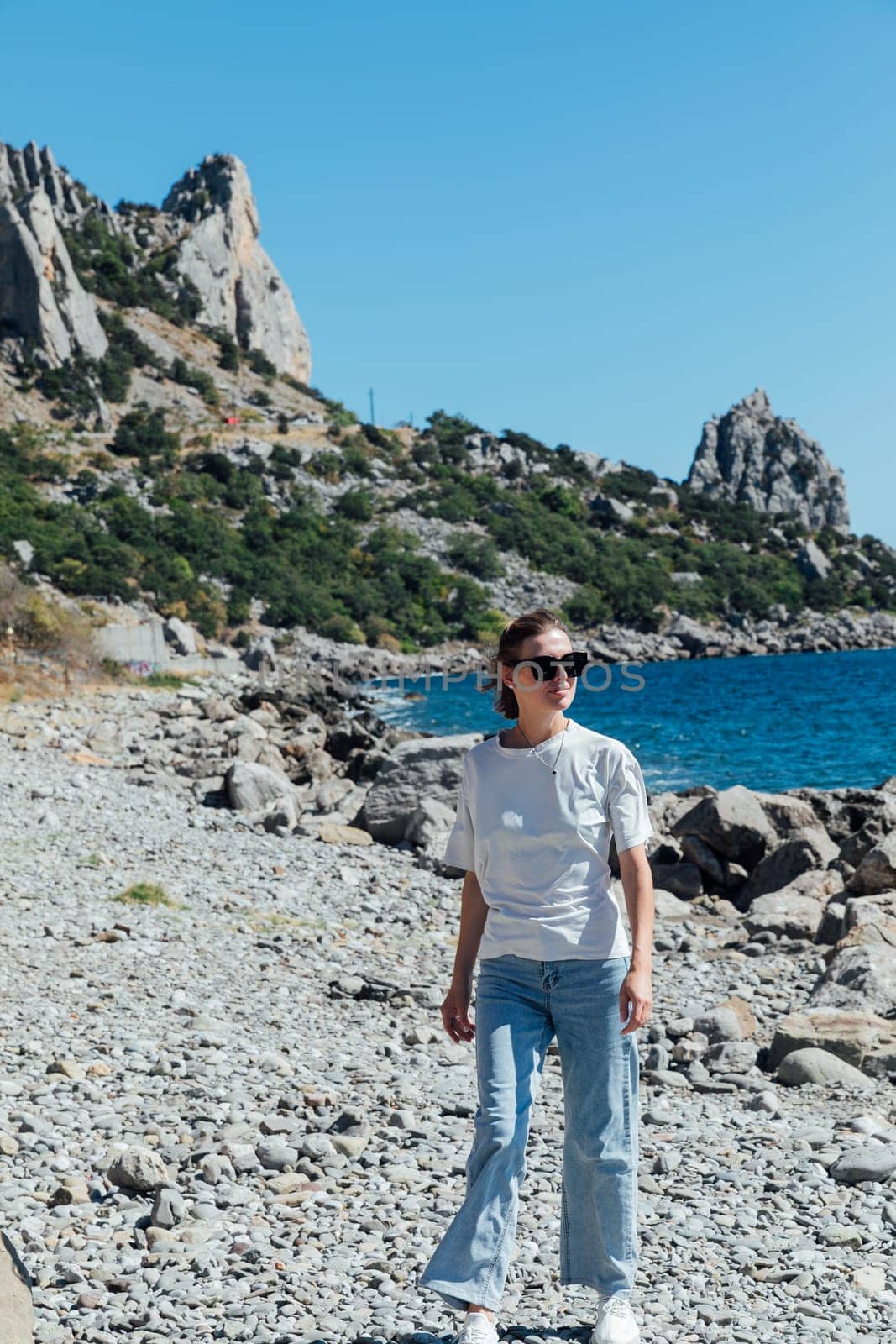 a woman in jeans stands on the seashore by the stones beach rest nature