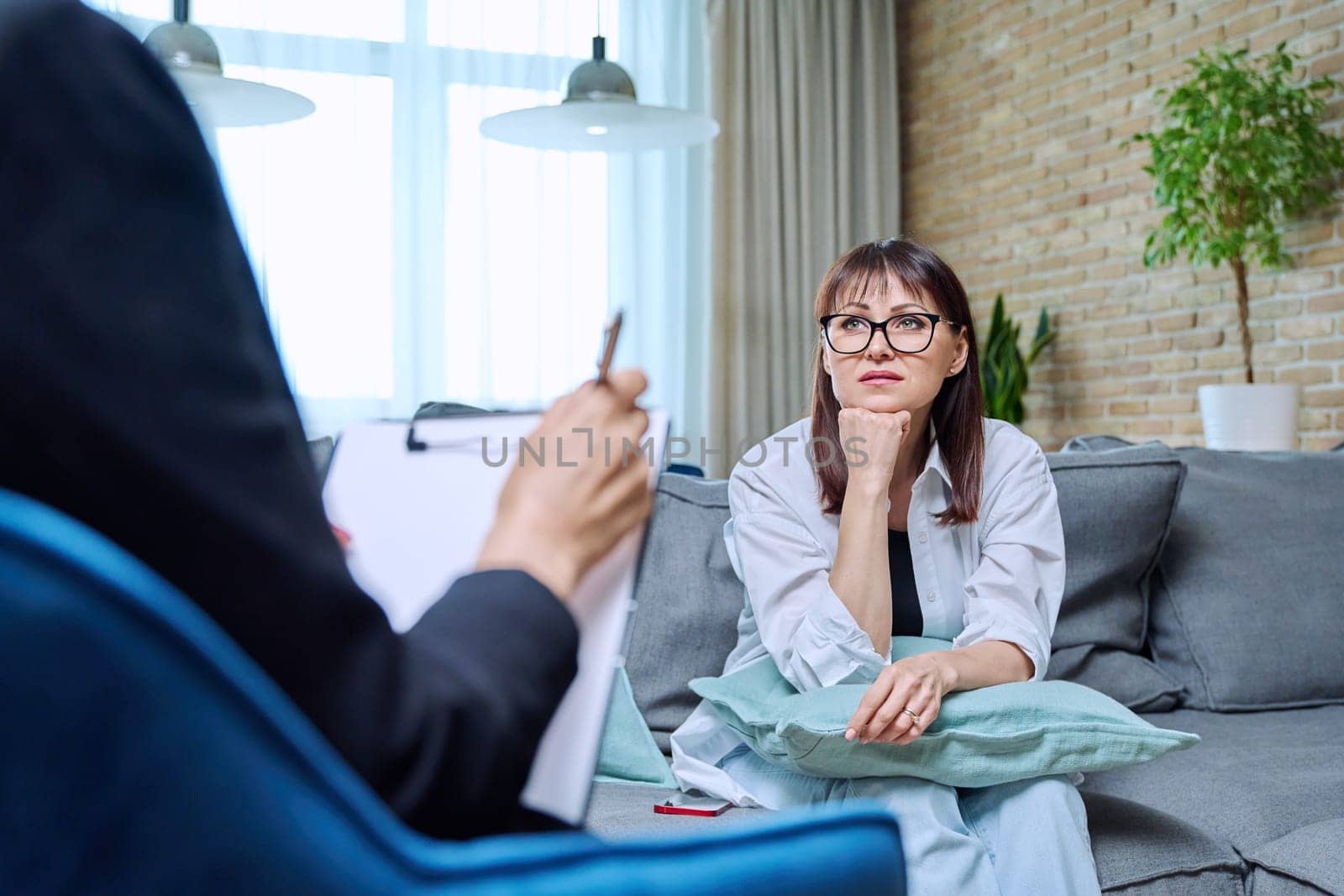 Middle-aged woman at meeting with psychologist counselor, sitting on couch in office. Mental problems of age female, psychological support help. Psychology psychotherapy therapy treatment healthcare