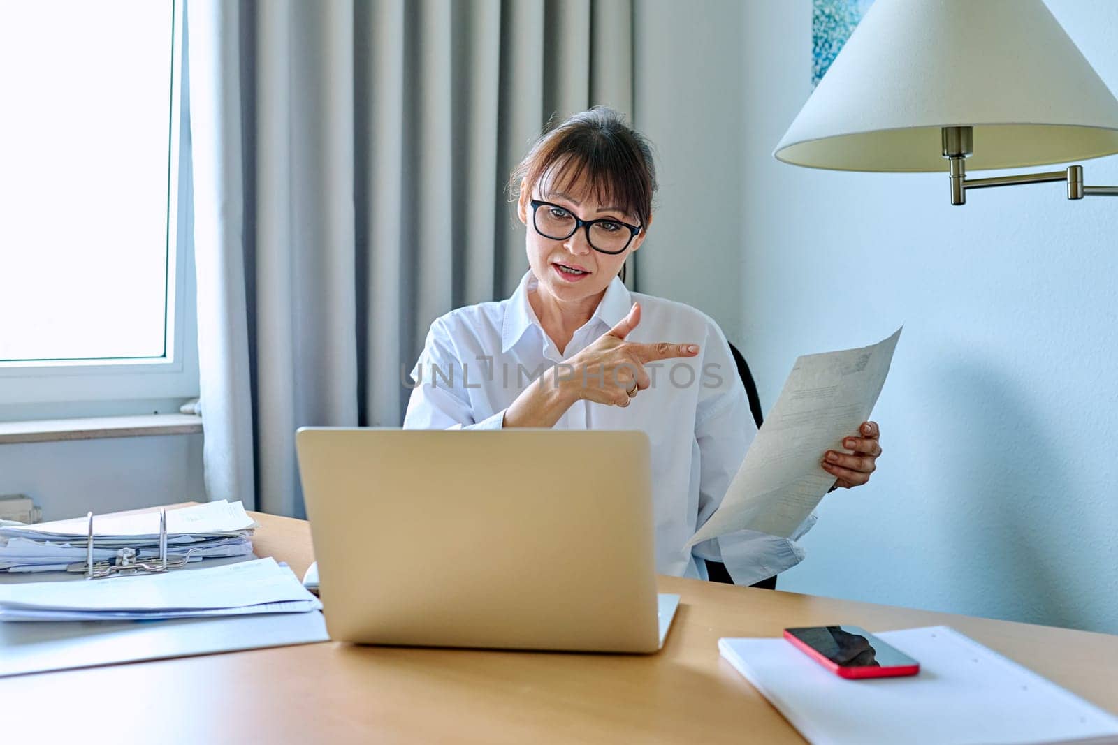 Mature business woman working remotely, having an online chat conference, in home office. Female manager accountant mentor teacher freelancer talking on video call on laptop computer with clients