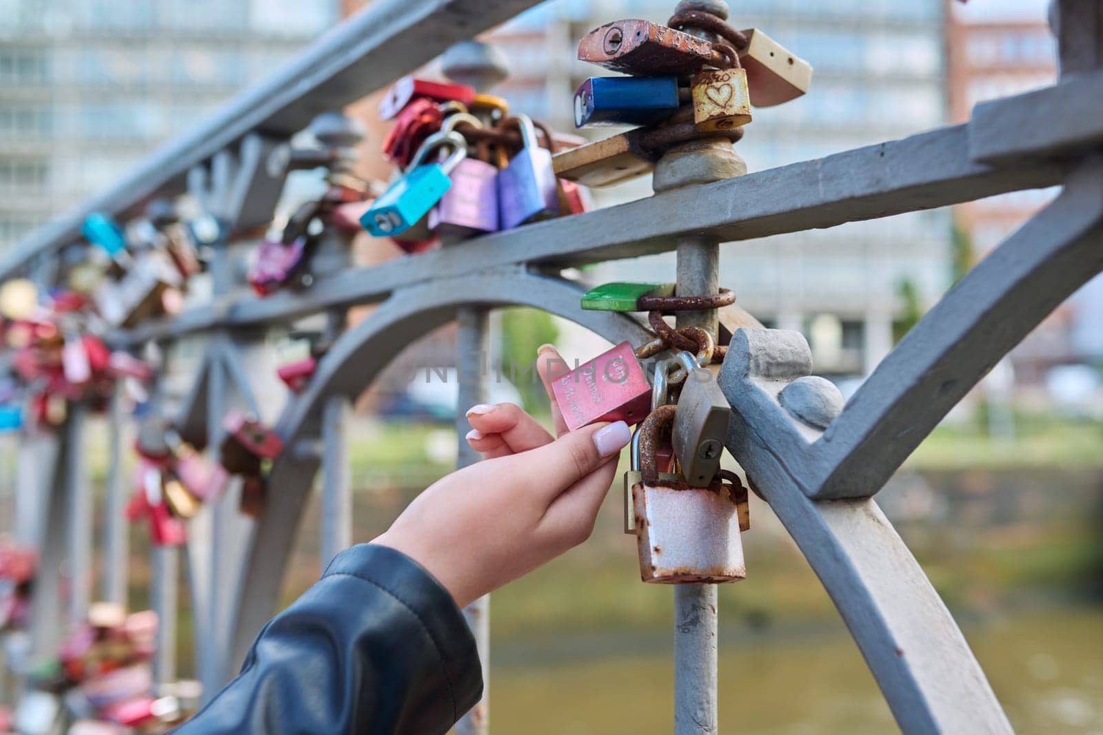 Hamburg, Germany, 1.08.2023, many closed heart love locks on the bridge, woman's hand holding her love padlock, close up. Romantic symbols signs