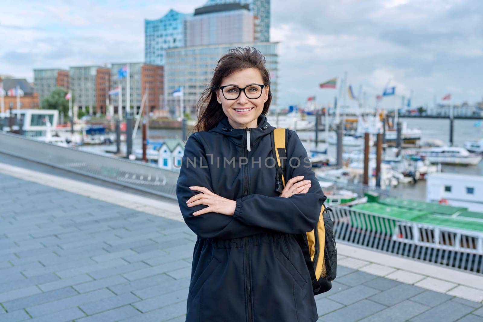 Mature woman tourist in Hamburg, posing in river port, against backdrop of Elbphilharmonie Hamburg, modern Concert Hall