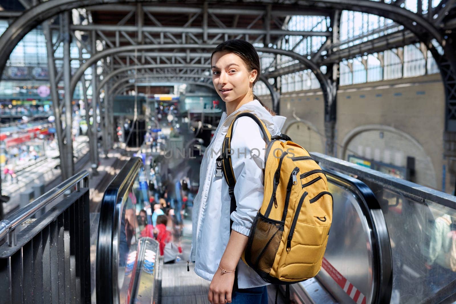 Teenage girl with backpack looking at camera at railway station. High school student, teenager girl passenger, suburban urban and intercity rail transport