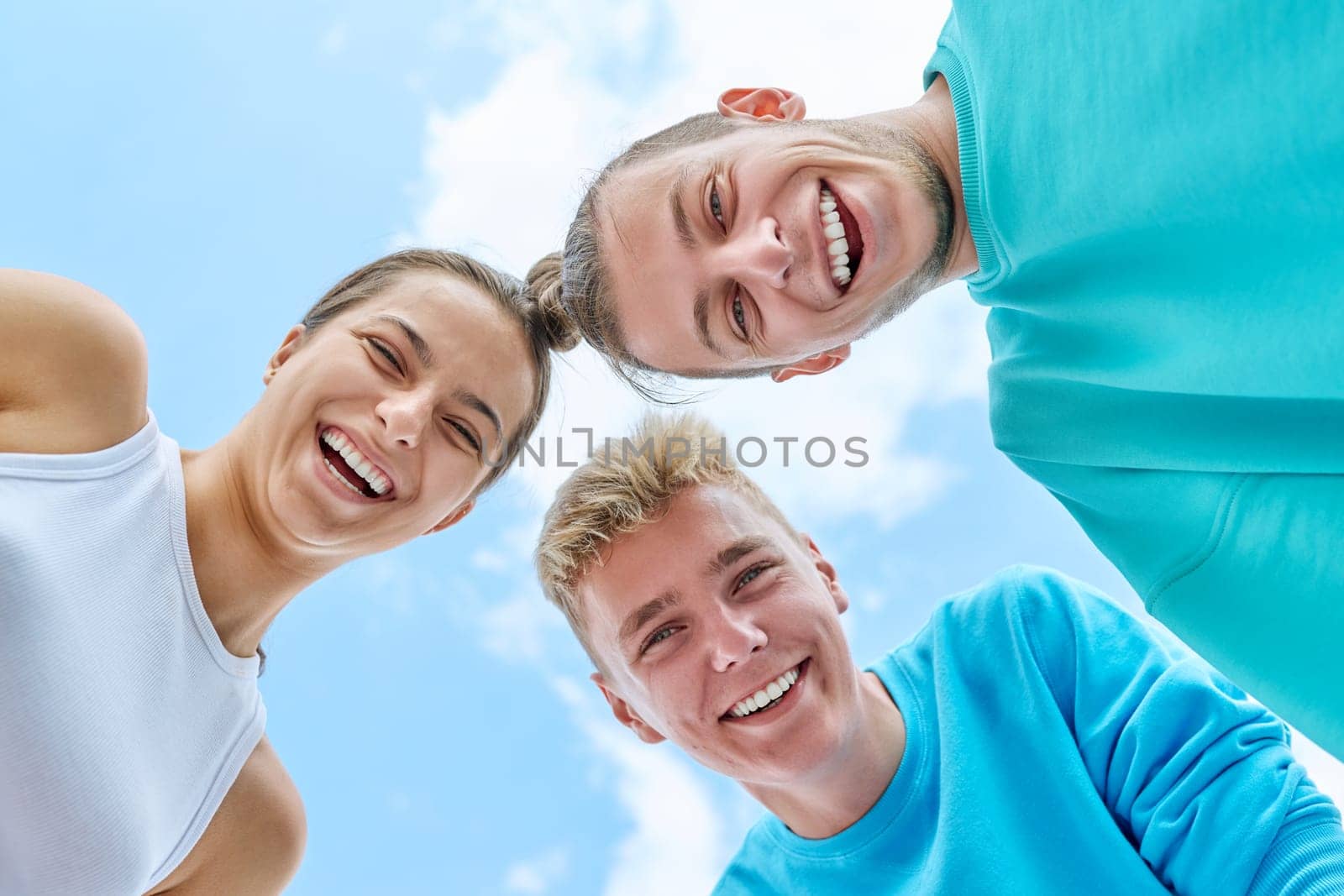 Closeup faces of young teenage guys and girl laughing looking down at camera, blue sky with clouds background. Youth, team summer vacation, communication leisure friendship fun lifestyle holiday