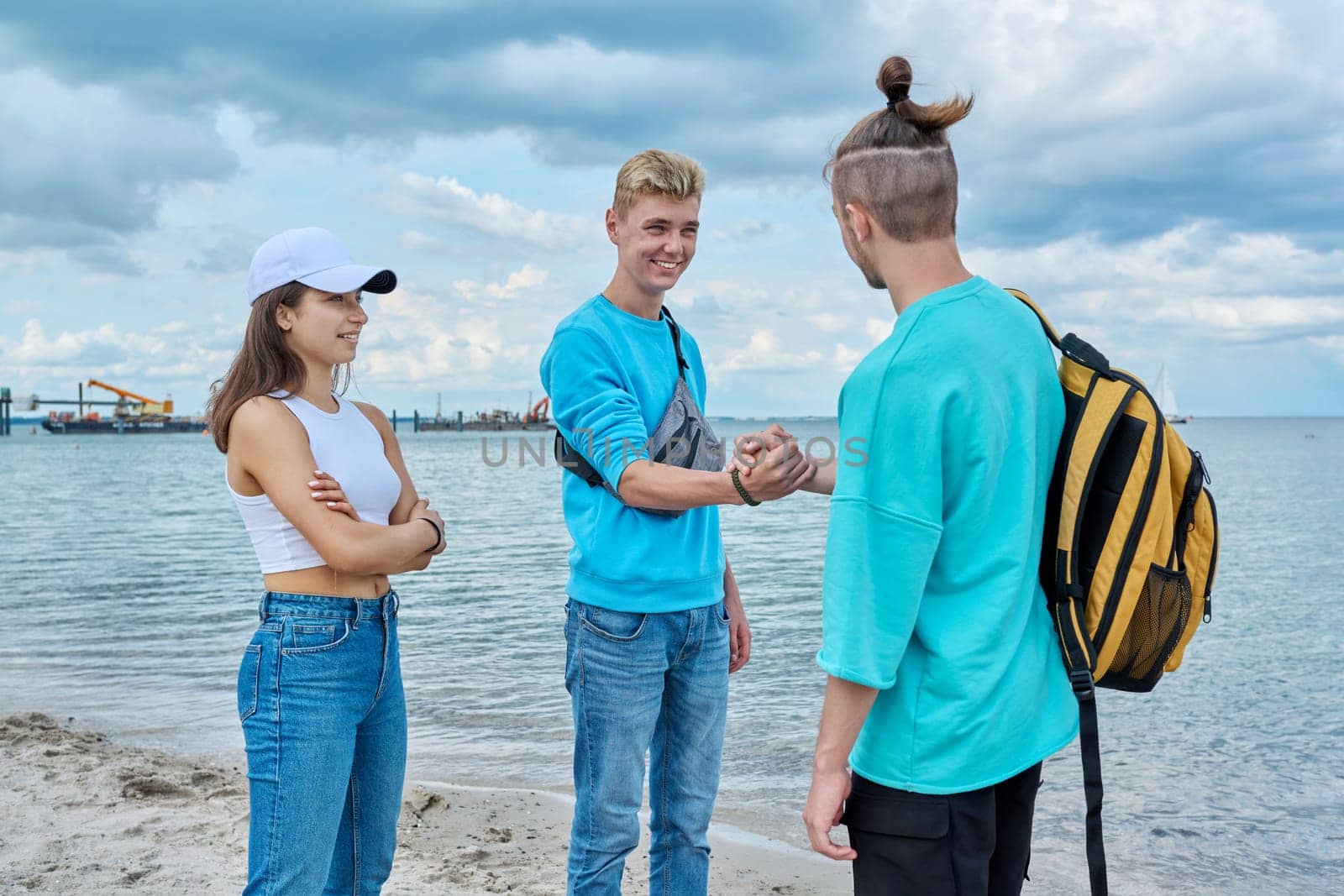 Young teenage friends guys and girl meeting, greeting, shake hands on beach by VH-studio