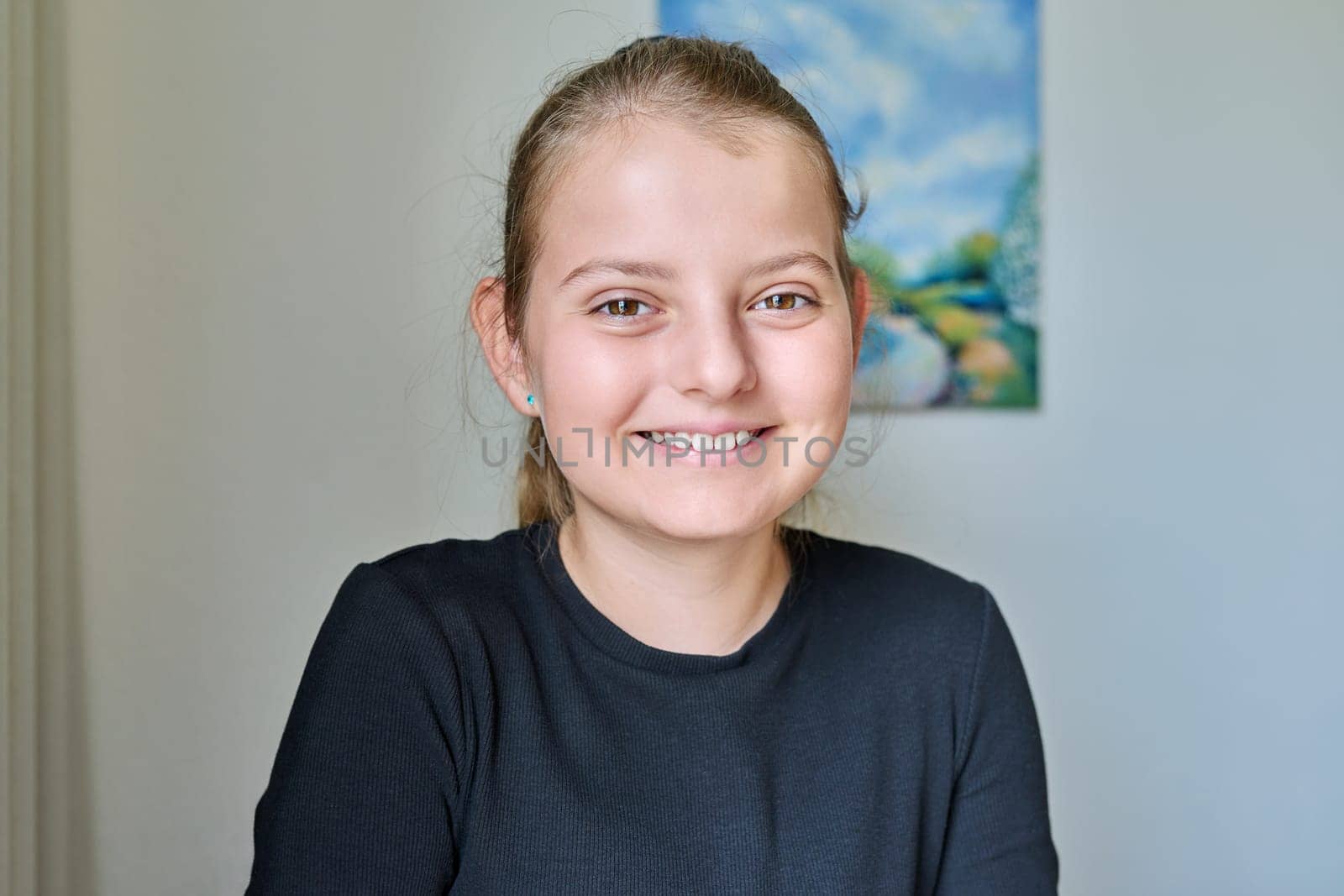 Headshot portrait of happy smiling child girl 10 years old inside on background of light wall