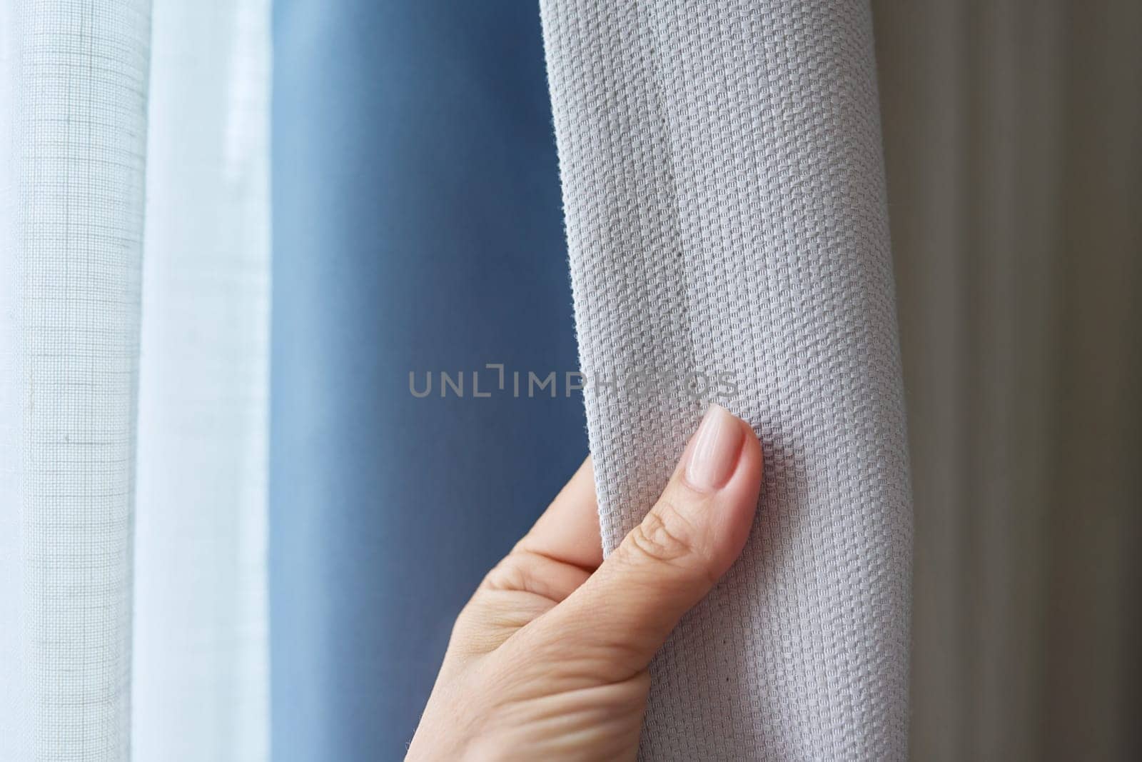 Close-up of woman's hand showing light gray curtain on blue opaque lining, fabric blackout