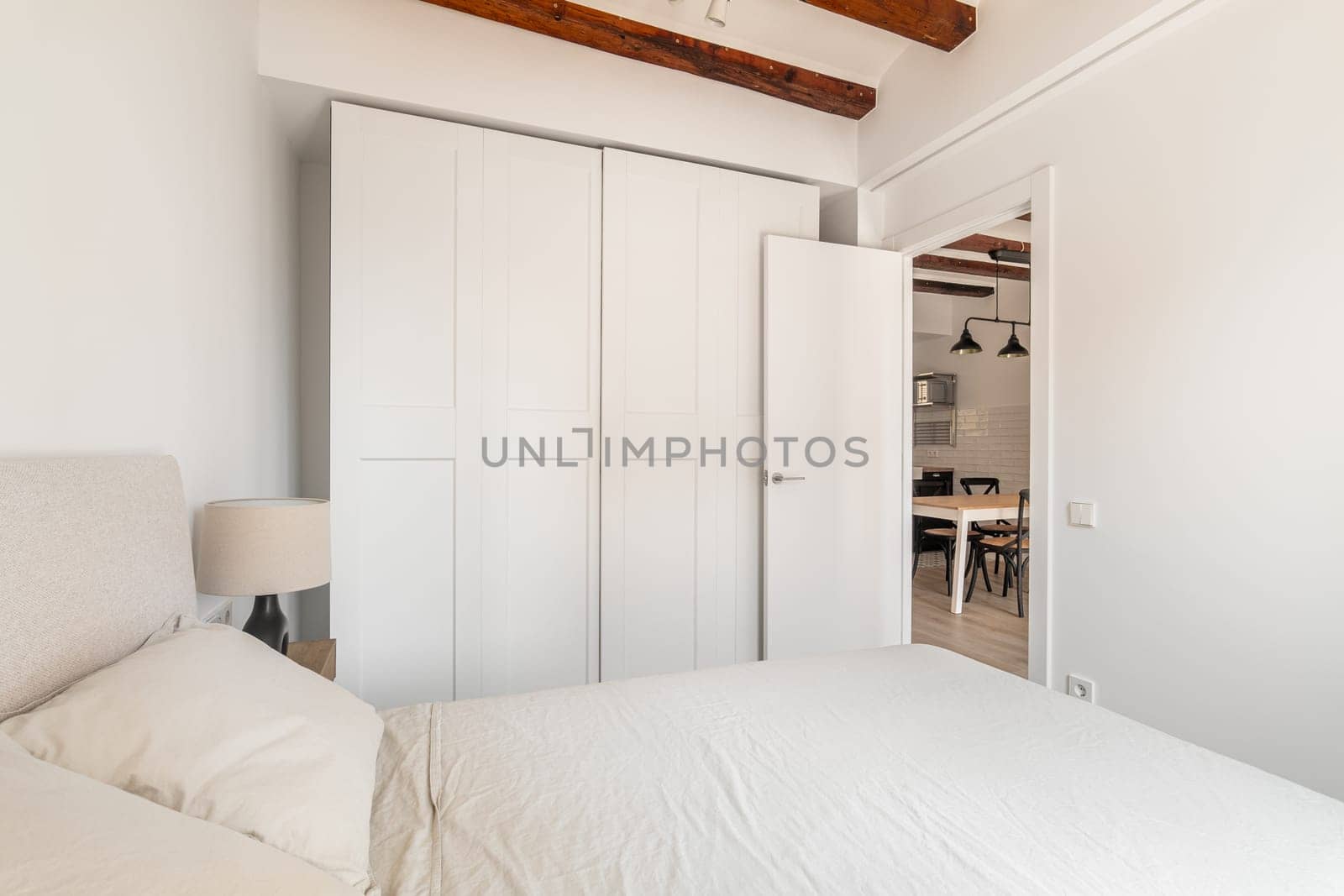 Large wardrobe and soft double bed in white minimalist bedroom. Renovated apartment interior with place to rest and furniture. House design