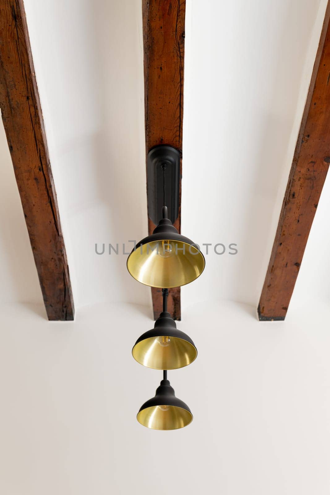 Stylish metal chandelier with light-bulbs on wooden ceiling beam. Contemporary light equipment for interior design and enclosure decor