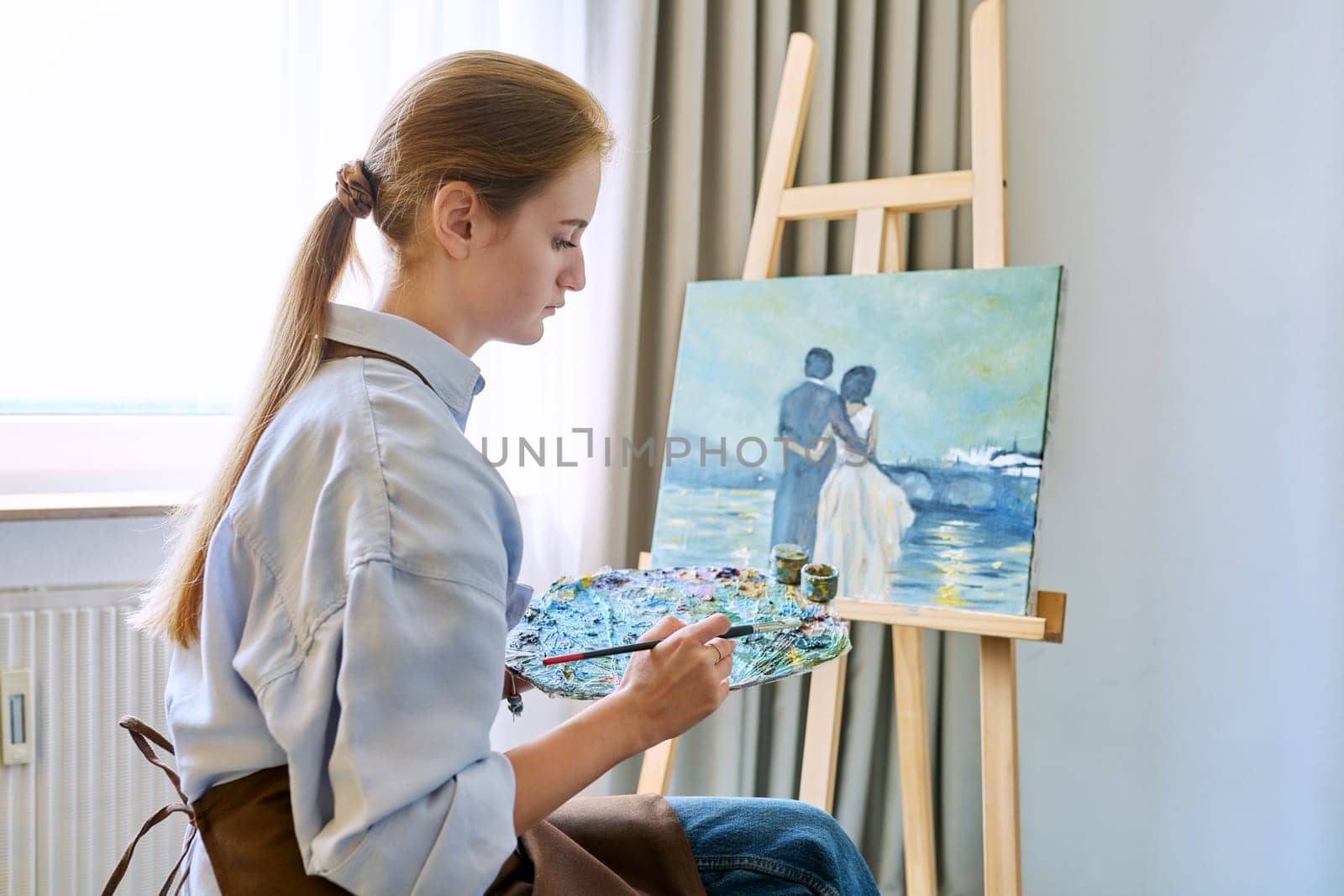 Young pretty female artist painting with acrylics on an easel by VH-studio
