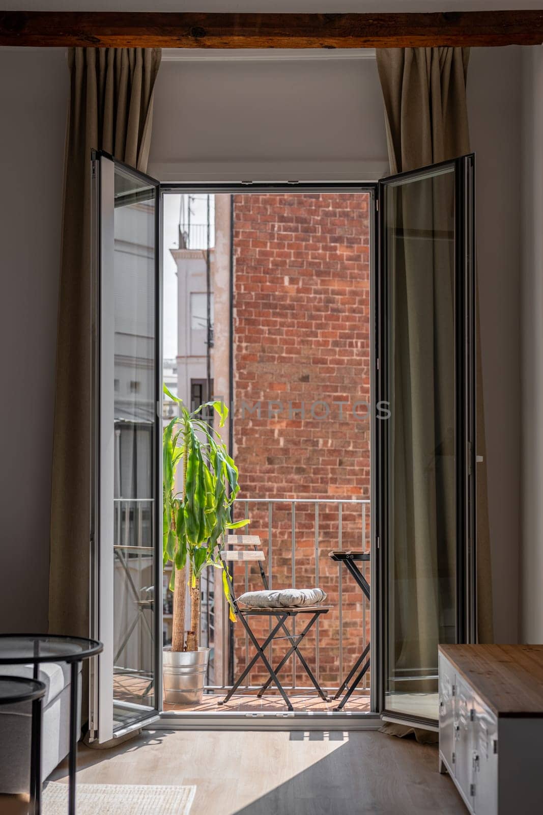 Open glass door of comfortable terrace with table and chair in renovated flat. Cosy place to rest on apartment balcony in Barcelona city