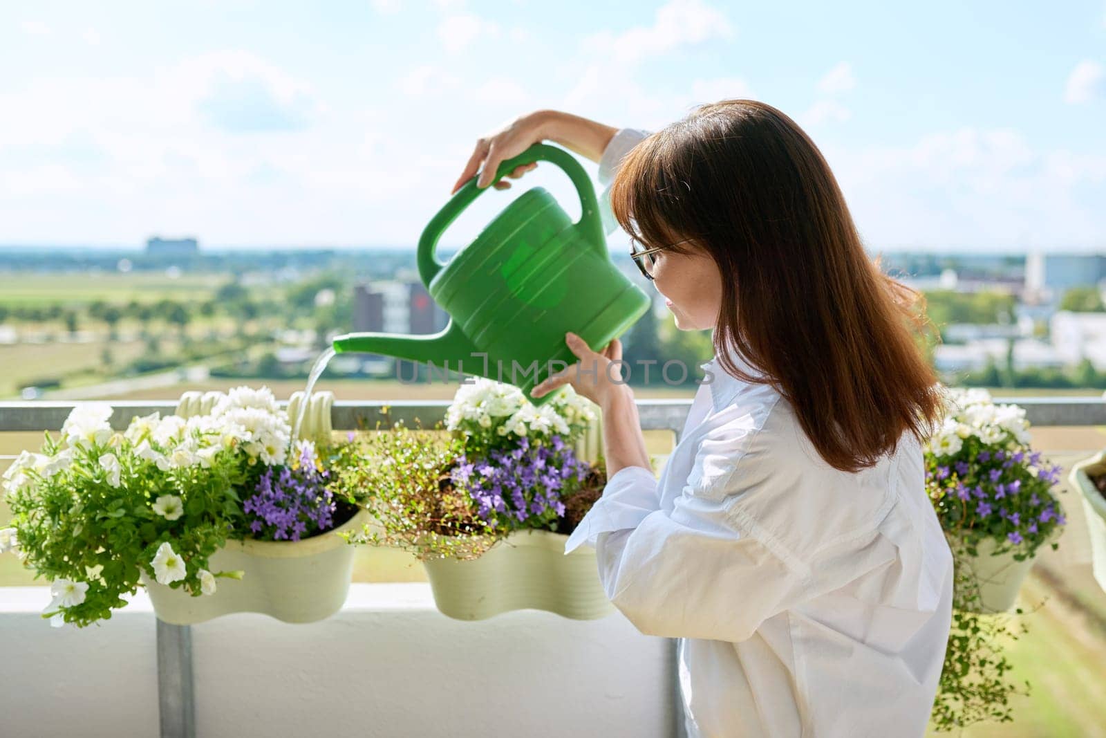 Woman watering potted plants from watering can on outdoor terrace at home. Green hobby, home gardening, eco trends