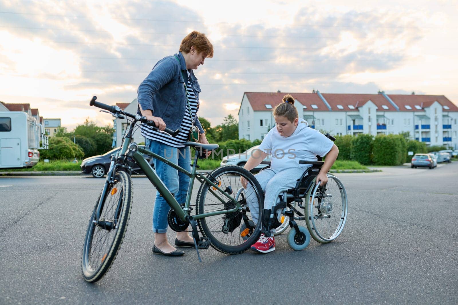 Boy transfers from wheelchair to bicycle, mother helping child to transfer, activity rehabilitation health concept