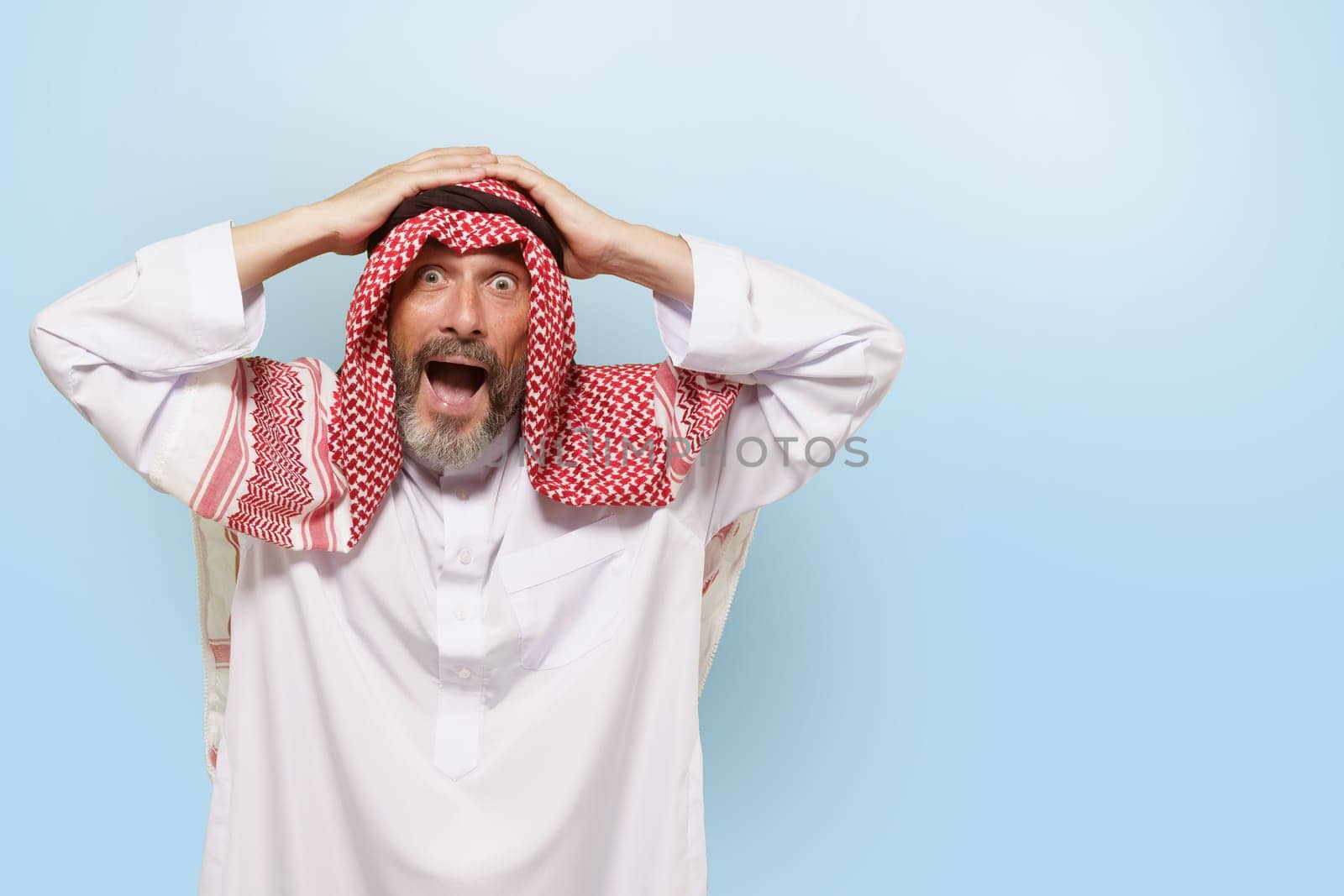 Excited Middle Eastern Arabian man, or Muslim, in traditional attire keffiyeh headscarf, with smile holds head. Joy and pride of Islamic people, cultural diversity and rich traditions of ethnic group. High quality photo