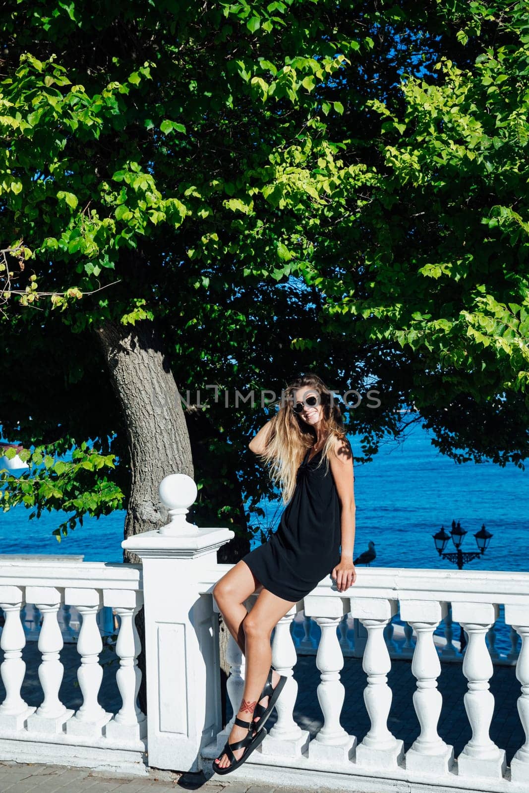 a woman in a black dress and stands by the railing near the sea in the park walk