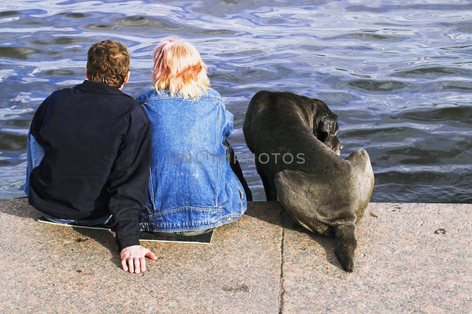 A couple and a dog sitting at the embankment of Neva river in Saint Petersburg,