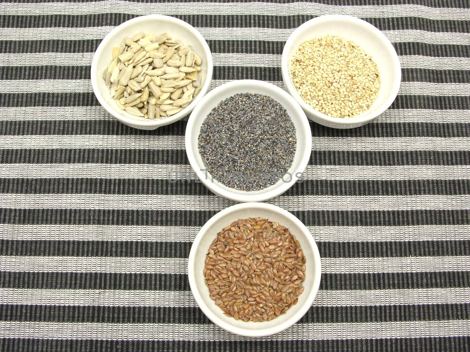Four bowls with different seeds on a striped background