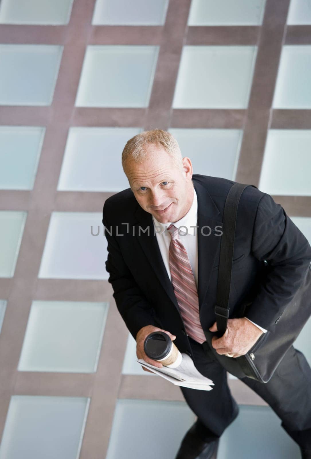 Businessman with briefcase holding paper and coffee cup. Vertically framed shot.