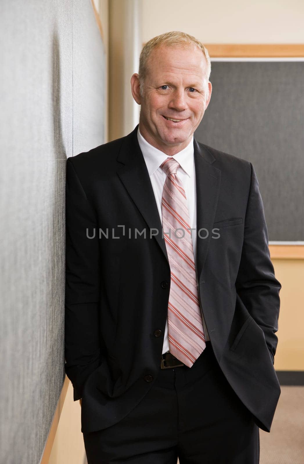 Smiling businessman leaning against wall. Vertically framed shot.