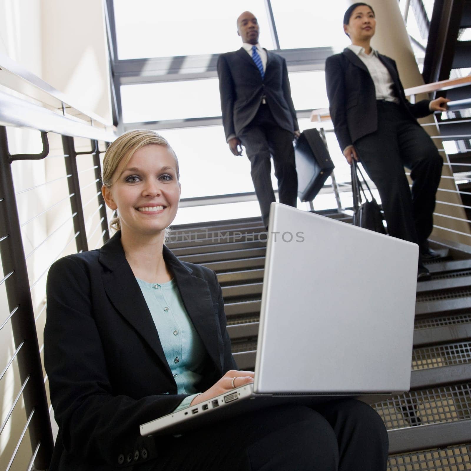 Businesswoman sitting on busy stairs with laptop. Square framed shot.