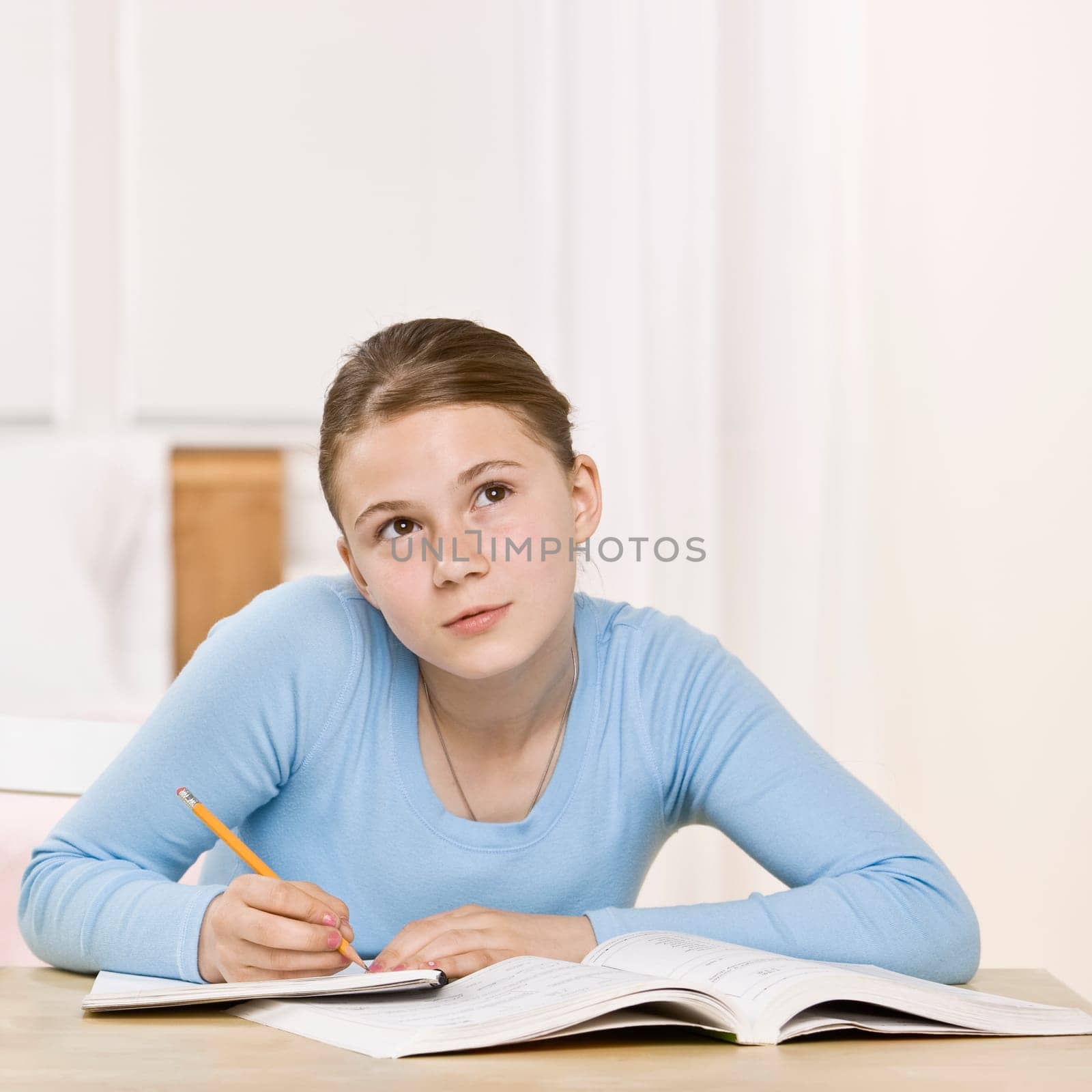 Young girl sitting at table doing homework. Square framed shot.