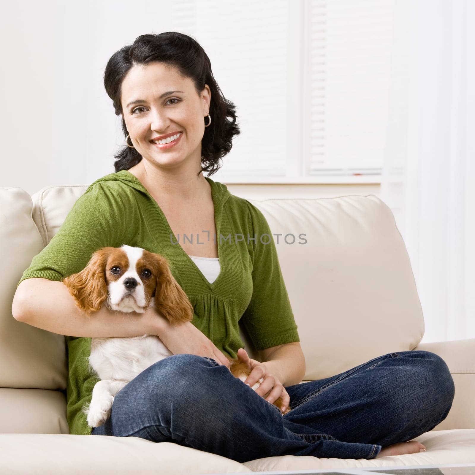 Woman sitting on couch holding puppy. Square format.