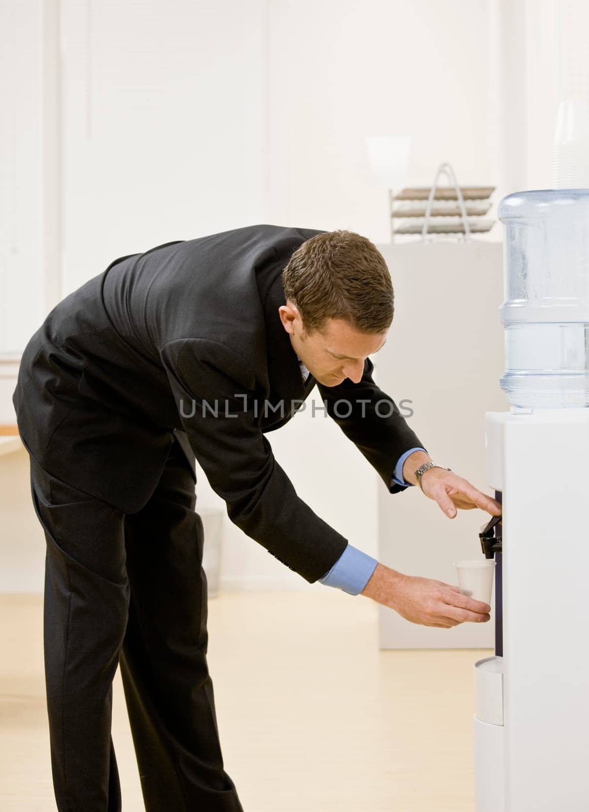 Business man getting water from water cooler. Vertically framed shot.
