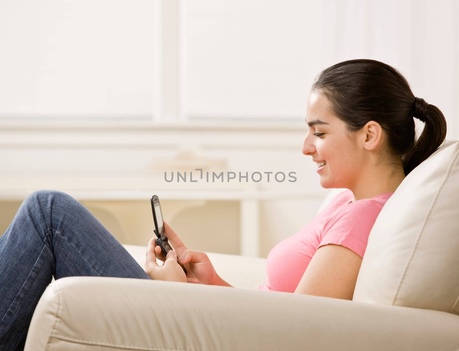 Young woman sitting on couch and using cellphone. Horizontally framed shot.