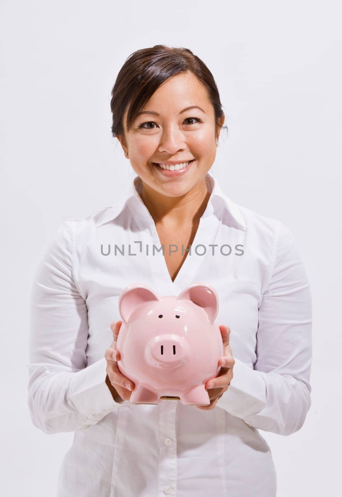 A beautiful and young asian woman holding a piggy bank. She is smiling at the camera. Vertically framed shot.