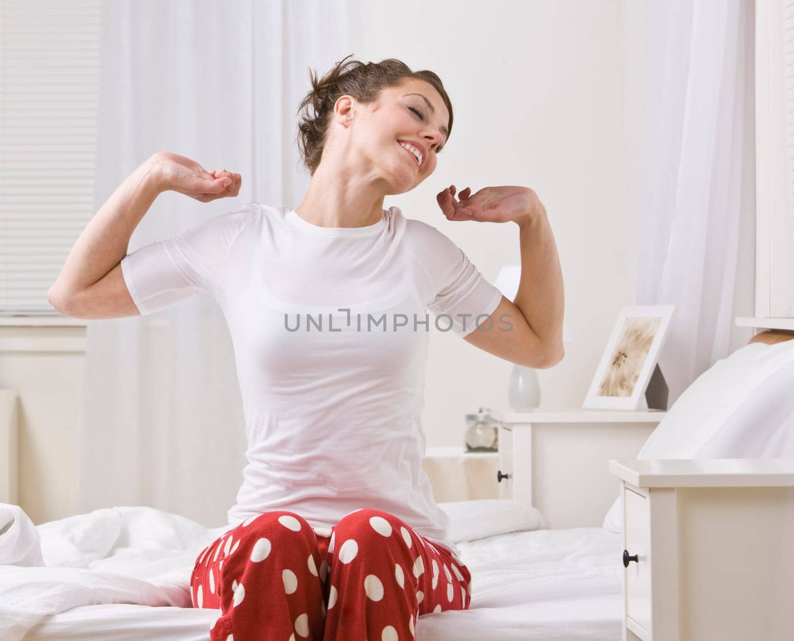 An attractive young woman stretching while sitting up in bed. She is smiling. Horizontally framed shot.