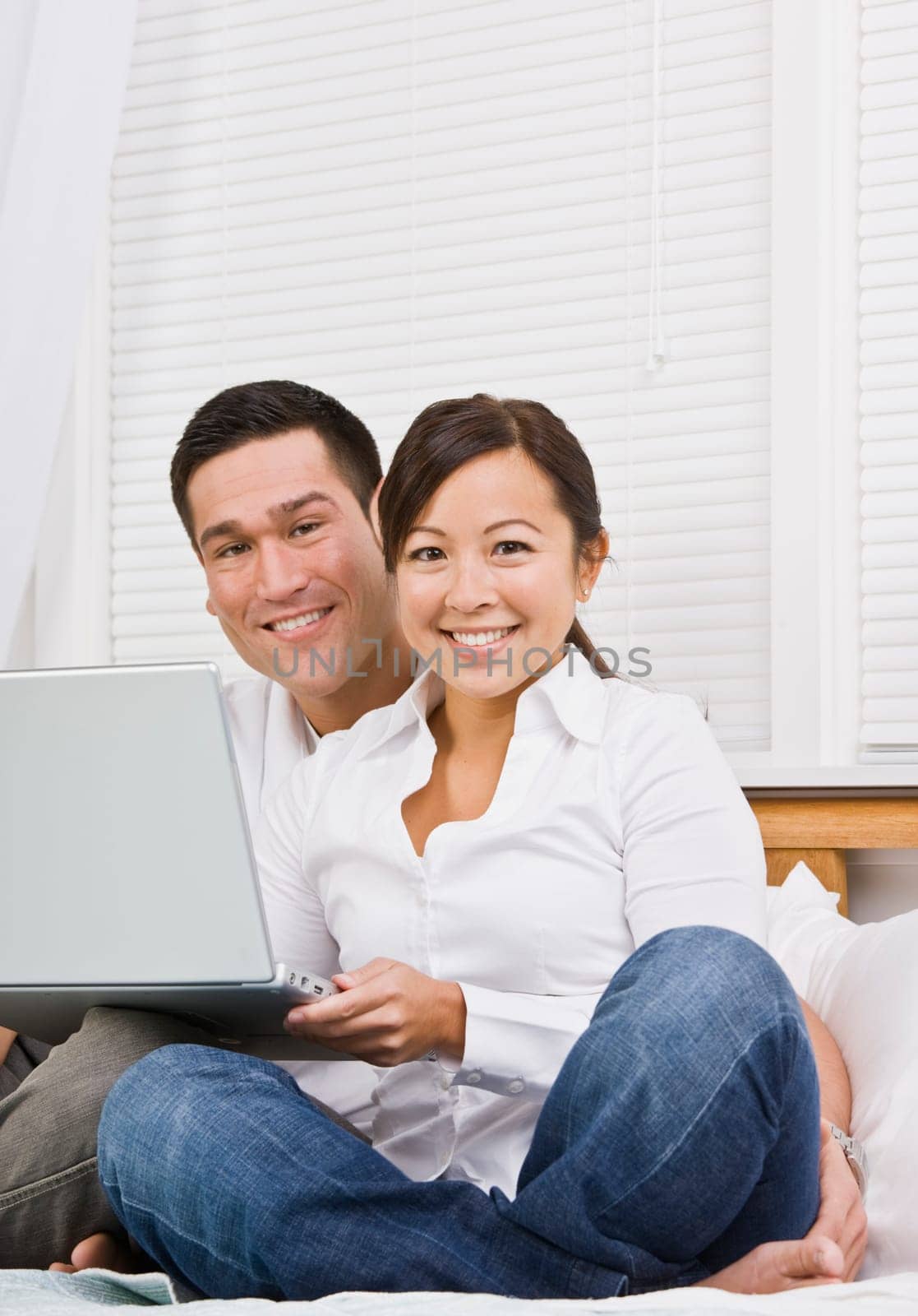 Attractive Asian couple sitting together with laptop. Vertically framed shot.